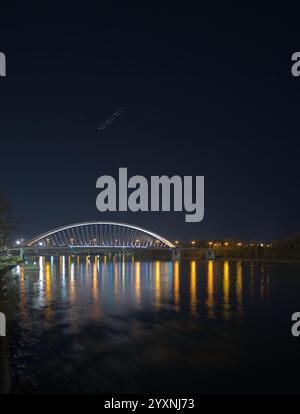 Eine hell beleuchtete moderne Brücke bei Nacht mit farbenfrohen Reflexen auf dem Fluss vor einem klaren dunklen Himmel. Stockfoto