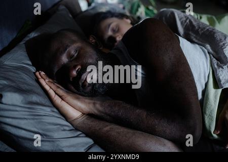Mittlere Nahaufnahme eines afroamerikanischen Mannes, der ruhig schläft, während seine Frau ihn umarmt Stockfoto