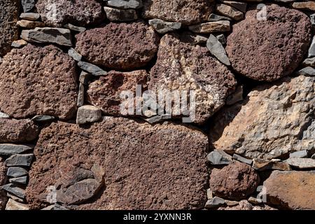 Eine Wand aus großen Felsen mit einer rauen Textur. Die Mauer besteht aus vielen verschieden großen Felsen, von denen einige größer sind als andere Stockfoto