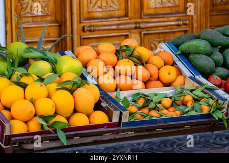 Eine Vielzahl von Obst und Gemüse wird auf einem Holztisch ausgestellt. Die Orangen sind in einer Kiste und die Avocados in einer separaten Kiste. Der Tisch ist Stockfoto