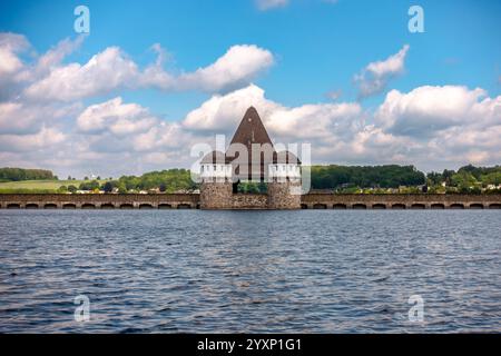 Ein großes Gebäude mit einem spitzen Dach steht auf einem Gewässer. Das Wasser ist ruhig und der Himmel ist klar Stockfoto