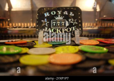 Ein Stapel farbenfroher Plastikmünzen mit einem Royal Jackpot Logo auf einer davon. Die Münzen sind auf einem Tisch verstreut, wobei einige davon auf der Oberseite o liegen Stockfoto