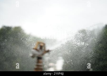 Ein Mann sprüht Wasser aus einem Schlauch. Das Wasser sprüht in die Luft, und der Mann steht in der Mitte. Die Szene ist verschwommen und das Wasser d Stockfoto