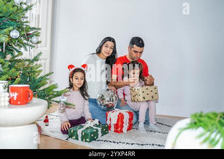 Die Familie genießt eine schöne Zeit in der Nähe des geschmückten Weihnachtsbaums. Die Kinder packen Geschenke aus, spielen und genießen die festliche Atmosphäre des Weihnachtsfestes Stockfoto