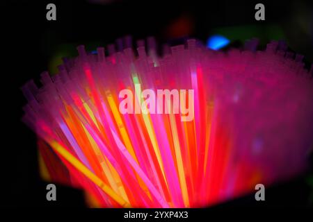 In einem dunklen Raum werden neonfarbene Kunststoffhalme beleuchtet. Die hellen Farben und die leuchtenden Lichter schaffen eine unterhaltsame und energiegeladene Atmosphäre Stockfoto