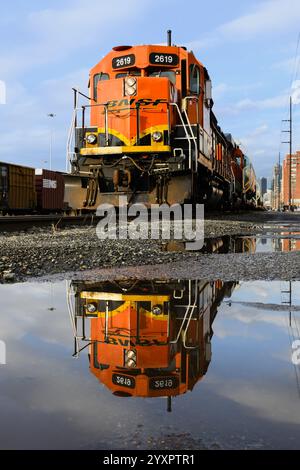 Seattle, WA, USA - 16. Dezember 2024; BNSF-Güterzug reflektiert in Pfütze bei Sonnenschein Stockfoto