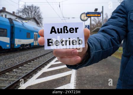 Bayern, Deutschland - 17. Dezember 2024: Eine Person hält ein Schild mit dem Text AUSSER BETRIEB vor einem Bahnhof und Gleisen. Symbolisches Bild für technische Störungen, defekte Züge oder unterbrochenen Bahnbetrieb. FOTOMONTAGE *** eine Person hält ein Schild mit dem Text AUSSER BETRIEB vor einem Bahnhof und Gleisen. Symbolbild für technische Störungen, defekte Züge oder unterbrochene Bahnbetriebsabläufe. FOTOMONTAGE Stockfoto