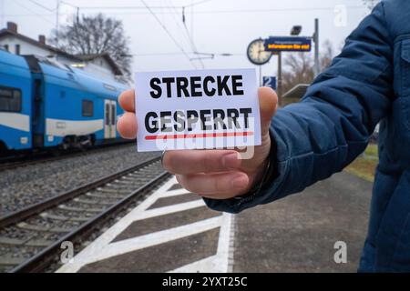 Bayern, Deutschland - 17. Dezember 2024: Eine Person hält ein Schild mit dem Text STRECKE GESPERRT vor einem Bahnhof und Gleisen. Symbolbild für Streckensperrungen, Bauarbeiten oder Unfälle im Schienenverkehr. FOTOMONTAGE *** eine Person hält ein Schild mit dem Text STRECKE GESPERRT vor einem Bahnhof und Gleisen. Symbolbild für Streckensperrungen, Bauarbeiten oder Unfälle im Schienenverkehr. FOTOMONTAGE Stockfoto