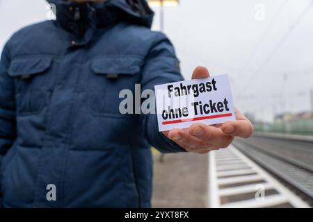 Bayern, Deutschland - 17. Dezember 2024: Eine Person hält ein Schild mit dem Text Passagier ohne Ticket. Symbolisches Bild für Fahrpreisumgehung, Ticketkontrollen und Strafmaßnahmen im öffentlichen Verkehr. FOTOMONTAGE *** eine Person hält ein Schild mit dem Text Fahrgast ohne Ticket. Symbolbild für Schwarzfahren, Ticketkontrollen und Strafen im öffentlichen Nahverkehr. FOTOMONTAGE Stockfoto