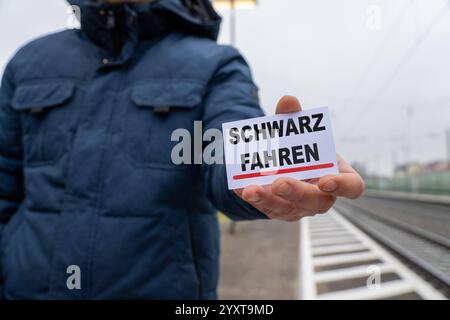 Bayern, Deutschland - 17. Dezember 2024: Eine Person hält ein Schild mit dem Text SCHWARZ FAHREN. Symbolisches Bild für Fahrkartenflucht, Ticketkontrollen und Bußgelder im öffentlichen Verkehr. FOTOMONTAGE *** eine Person hält ein Schild mit dem Text SCHWARZ FAHREN. Symbolbild für Schwarzfahren, Ticketkontrollen und Bußgelder im öffentlichen Nahverkehr. FOTOMONTAGE Stockfoto