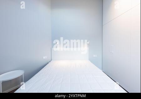 Helles und sauberes Schlafzimmer mit gemütlichem Bett, weißem Einbauschrank, Oberlicht und minimalistischem Design, Atmosphäre für perfekte Entspannung. Modern Min Stockfoto