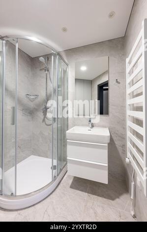 Modernes Bad mit verglaster Dusche, elegantem weißem Waschbecken, grauen gefliesten Wänden und modernen Annehmlichkeiten in einem ordentlichen und minimalistischen Ambiente Stockfoto