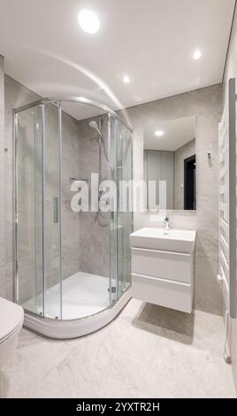 Modernes Bad mit verglaster Dusche, elegantem weißem Waschbecken, grauen gefliesten Wänden und modernen Annehmlichkeiten in einem ordentlichen und minimalistischen Ambiente Stockfoto