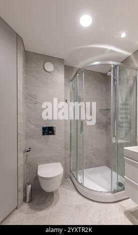Modernes Bad mit verglaster Dusche, elegantem weißem Waschbecken, grauen gefliesten Wänden und modernen Annehmlichkeiten in einem ordentlichen und minimalistischen Ambiente Stockfoto