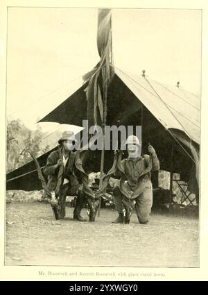 Afrikanische Wildwege, 1910, Jagd, Uganda, Beschreibung und Reise, Afrika Ost, in einer historischen Szene knieten zwei Männer, beide in Militärkleidung, stolz neben ihren Gewehren. Sie befinden sich vor einem großen Zelt, was auf eine Zeltumgebung hinweist und mit einer hochgezogenen Fahne geschmückt ist. Die Kulisse bietet eine zerklüftete Landschaft, die auf die Wildnis um sie herum hinweist. Ein Mann strahlt ein Gefühl von Führung und Selbstvertrauen aus, während er enthusiastisch Gesten ausübt, während der andere aufrecht steht und ein starkes und entschlossenes Verhalten zeigt. Dieser Moment fängt den Geist des Abenteuers und der Kameradschaft ein Stockfoto