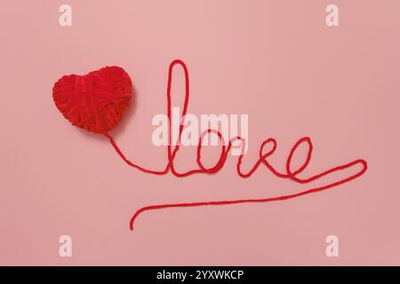 Herzförmiger Garnball mit „Love“-Wort auf rosa Hintergrund Stockfoto