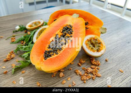 Papaya-Frucht, Passionsfrucht, Rucola und Müsli auf hellem hölzernem Hintergrund. Scheiben süßer Papaya, Maracuja, grüner Rucola umgeben von Granola fla Stockfoto