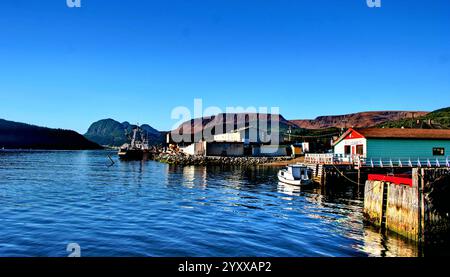 Eine malerische Küstenszene in Neufundland, Kanada, mit einem kleinen Boot, das von einer farbenfrohen Lounge mit bergigem Hintergrund angedockt wird. Stockfoto