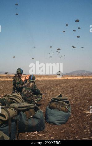 DF-ST-87-13308 Fallschirmjäger diskutieren über einen Flugabwurf, während andere Mitglieder der 1. Spezialkräfte und 40 US-Luftwaffe während des ÜBUNGSTEAMS SPIRIT '85 mit einem Fallschirm über Yoju fliegen. Stockfoto