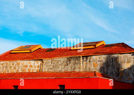 Gebäude mit einem leuchtend roten unteren Abschnitt und einem oberen Abschnitt aus Stein, gekrönt von einem rot gekachelten Dach. Das Dach verfügt über Dachfenster und den Himmel im bac Stockfoto