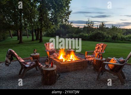 Gemütliches Feuerstellen bei Sonnenuntergang im Hinterhof mit grünem Gras und Bäumen im Hintergrund Stockfoto