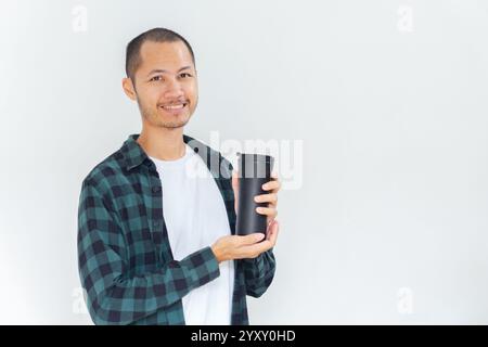 Junge asiatische Männer, die Flanell und Hemd tragen, halten schwarzen Tumbler mit einem Lächeln auf isoliertem weißen Hintergrund Stockfoto