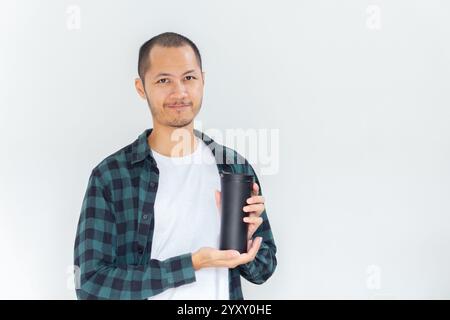 Junge asiatische Männer, die Flanell und Hemd tragen, halten schwarzen Tumbler mit einem Lächeln auf isoliertem weißen Hintergrund Stockfoto