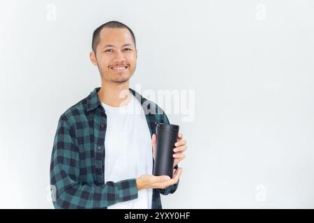 Junge asiatische Männer, die Flanell und Hemd tragen, halten schwarzen Tumbler mit einem Lächeln auf isoliertem weißen Hintergrund Stockfoto