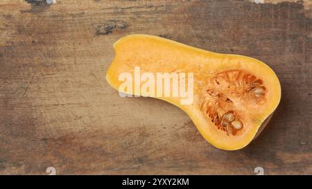Butternusskürbis, der in zwei Hälften geschnitten ist, enthüllt lebendiges Orangenfleisch und Samen auf Schneidebretthintergrund, von oben mit Kopierraum aufgenommen Stockfoto
