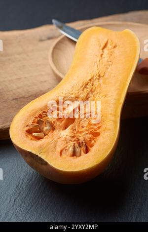 In zwei Hälften geschnittener Butternusskürbis enthüllt lebendiges orangefarbenes Fleisch und Samen auf dem Schneidebrett mit Messer und Holzschale im Hintergrund, weicher Fokus mit Kopie Stockfoto