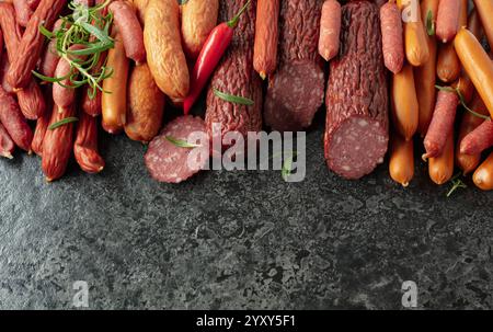 Verschiedene Trocken- und Räucherwürste mit roter Paprika und Rosmarin auf einem Steintisch. Draufsicht, Kopierraum. Stockfoto