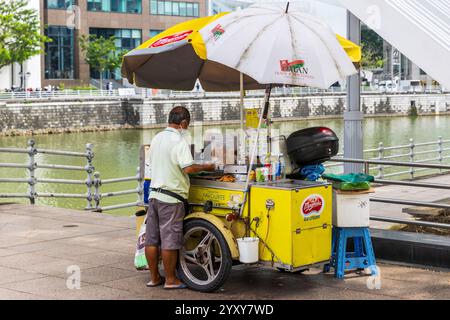 Der Straßenverkäufer bereitet Snacks auf einem gelben Wagen am Flussufer in Singapur zu. Foto: David Rowland / One-Image.com Stockfoto
