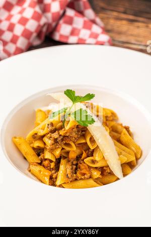 Blick von oben auf Penne Bolognese Pasta auf weißem Teller auf Holztisch Stockfoto