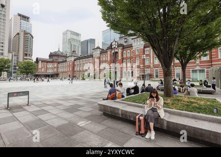 Passagiere mit Gepäck, die auf einer Bank unter einem Baum auf dem Marunouchi-Platz neben dem Bahnhof Tokio im Geschäftsviertel Marunouchi sitzen, Tokio, Japan, Stockfoto