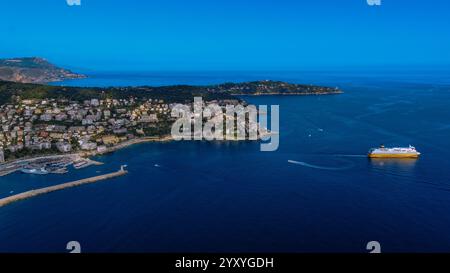 Atemberaubende Luftaufnahme einer Küstenstadt, umgeben von üppigem Grün und klarem blauem Meer, mit einer Fähre, die in ruhigem Mittelmeer fährt. Stockfoto