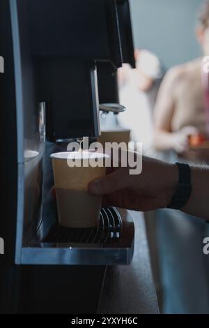 Männliche Hand nimmt an der Hotelrezeption eine Papiertasse mit Kaffee aus der Kaffeemaschine. Stockfoto