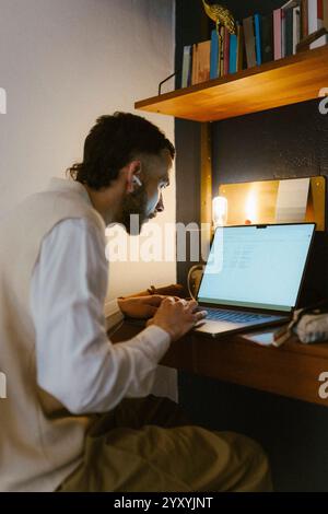 Der zielgerichtete Freelancer trägt kabellose in-Ear-Kopfhörer, während er zu Hause am Notebook arbeitet Stockfoto