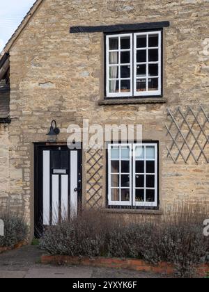 Fassade des Primrose Cottage im Dorf Yardley Hastings, Northamptonshire, Großbritannien; markante schwarz-weiß gestreifte Eingangstür. Stockfoto