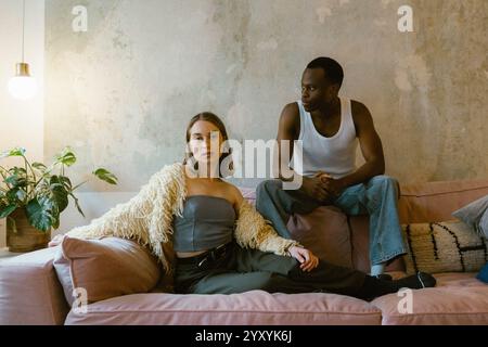 Selbstbewusste junge Frau, die auf dem Sofa sitzt, mit einem Freund in der Wohnung Stockfoto