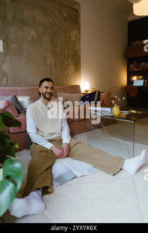 Volle Länge eines glücklichen Mannes in zwanglosem Sitzen mit Magazin in der Nähe des Sofas zu Hause Stockfoto