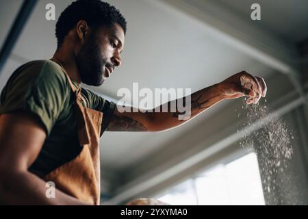 Niedriger Winkel des männlichen Bäckers, der Mehl während der Arbeit in der Bäckerei staubt Stockfoto