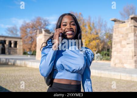 Junge schwarze Geschäftsfrau, die ihr Smartphone im debod-Tempel in madrid am sonnigen Tag benutzt Stockfoto