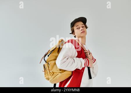 Der junge Mann zeigt seine trendige Bomberjacke, während er im Studio einen Rucksack trägt. Stockfoto