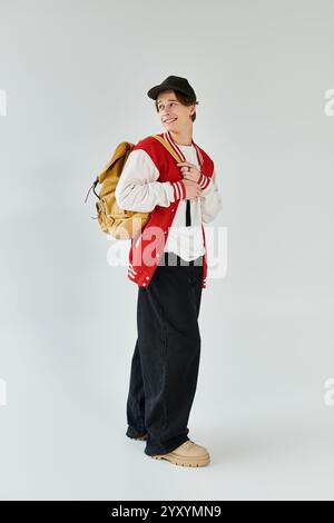 Ein hübscher junger Mann mit stylischer Bomberjacke und Rucksack steht selbstbewusst in einem Studio. Stockfoto