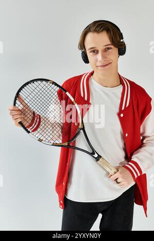 Ein hübscher junger Mann posiert mit einem Tennisschläger und trägt eine schicke Bomberjacke in einem Studio. Stockfoto