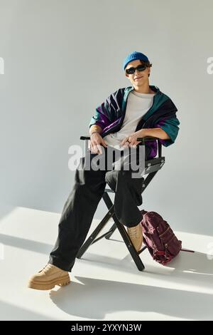 Ein gutaussehender junger Mann posiert selbstbewusst in einem Studio mit einer stylischen Bomberjacke und Sonnenbrille. Stockfoto