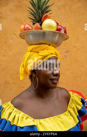 Eine Nahaufnahme Einer Palenquera-Frau in Einem traditionellen gelben Kleid, die Einen Obstkorb auf dem Kopf ausbalanciert. Stockfoto