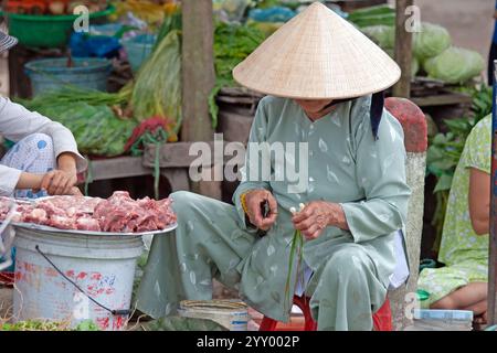 Vietnamesische Frau, die auf dem lokalen Markt Essen zubereitet, trägt tagsüber einen traditionellen konischen Hut Stockfoto