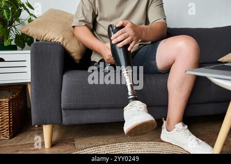 Ein hübscher junger Mann sitzt bequem auf einer Couch und konzentriert sich auf seine Beinprothese. Stockfoto