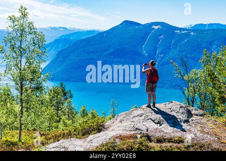 Ein Wanderer genießt die atemberaubende Aussicht auf einen norwegischen Fjord von einem Felsvorsprung. Die umliegenden Berge erheben sich majestätisch und schaffen eine ruhige Atmosphäre Stockfoto